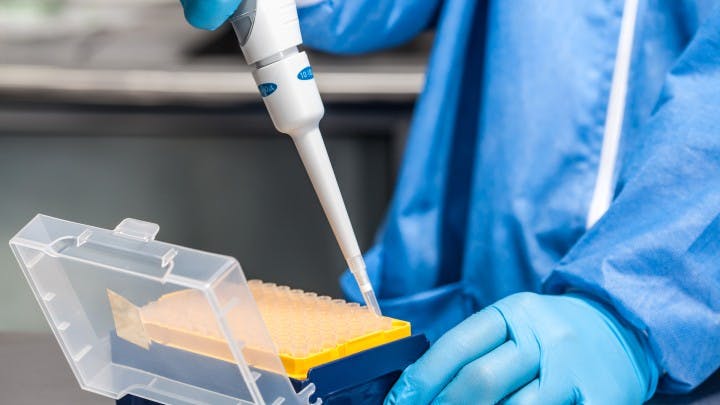Figure 1: A lab employee attaches a disposable tip to a pipette, which is used to dispense liquids in testing procedures.