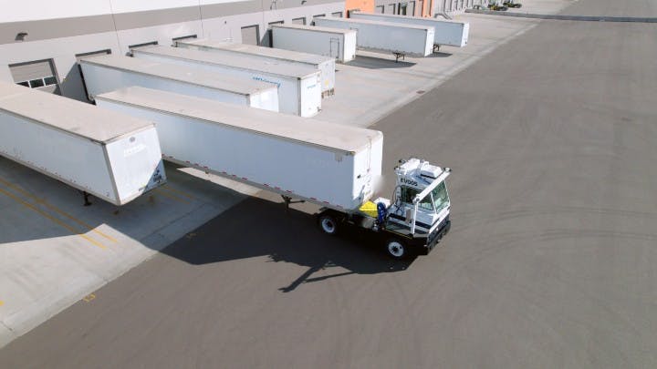 An autonomous yard truck, assisted by AI, backs a trailer to a loading dock.