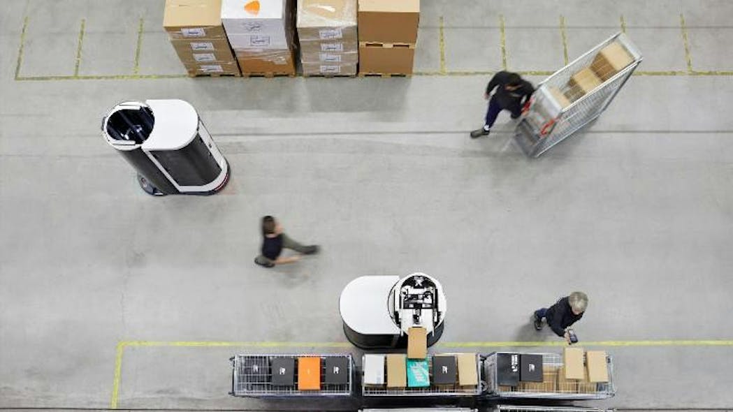 View from above of robots and humans at work. The robot in the front, center, is placing shoeboxes at a handover station for further processing by human co-workers.